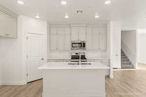 Kitchen featuring a center island with sink, sink, light wood-type flooring, and stainless steel appliances