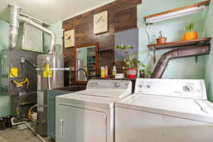 Laundry room featuring secured water heater, wood walls, sink, and washing machine and clothes dryer