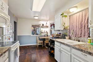 Kitchen with sink, white cabinets, dark wood-type flooring, and white appliances