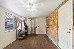 Workout room with ceiling fan, dark hardwood / wood-style flooring, a textured ceiling, and brick wall