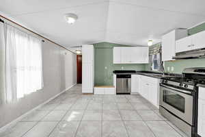 Kitchen featuring lofted ceiling, white cabinets, sink, light tile patterned floors, and stainless steel appliances