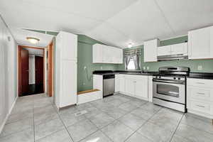 Kitchen featuring white cabinets, light tile patterned flooring, vaulted ceiling, and appliances with stainless steel finishes