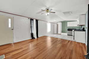 Unfurnished living room with light wood-type flooring, vaulted ceiling, a wealth of natural light, and ceiling fan