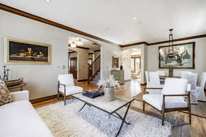 Living room featuring light wood-type flooring, crown molding, and a notable chandelier