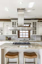 Kitchen with a breakfast bar, decorative backsplash, white cabinetry, and stainless steel gas stovetop