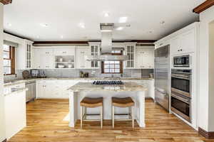 Kitchen featuring white cabinetry, light hardwood / wood-style flooring, built in appliances, a breakfast bar, and a kitchen island