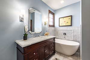 Bathroom featuring vanity, a bath, and tile walls