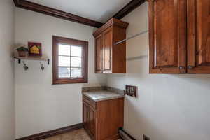 Laundry area featuring electric dryer hookup, crown molding, light tile patterned floors, and cabinets