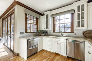 Kitchen with white cabinetry, sink, stainless steel dishwasher, and light hardwood / wood-style floors