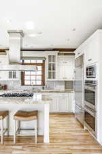 Kitchen with built in appliances, a breakfast bar, white cabinetry, and light hardwood / wood-style flooring