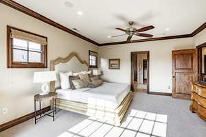 Carpeted bedroom with ceiling fan and crown molding