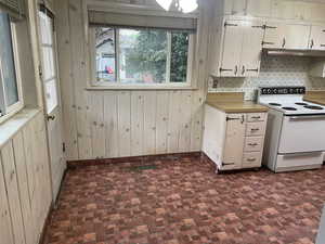 Kitchen with backsplash, wood walls, and white electric stove