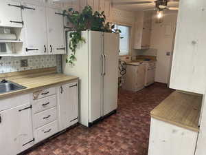 Kitchen featuring backsplash, ceiling fan, sink, white refrigerator, and white cabinets