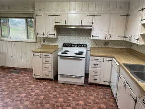 Kitchen with tasteful backsplash, wood walls, sink, and white appliances