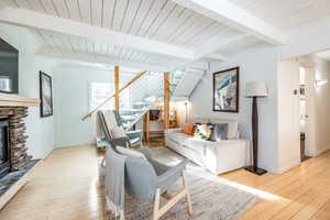 Living room featuring beam ceiling, light wood-type flooring, and a stone fireplace