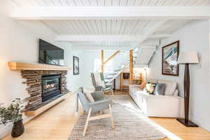 Living room with beamed ceiling, light hardwood / wood-style floors, a stone fireplace, and wood ceiling