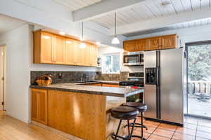 Kitchen with beam ceiling, sink, a breakfast bar, appliances with stainless steel finishes, and light wood-type flooring