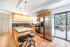 Kitchen featuring appliances with stainless steel finishes, light wood-type flooring, a kitchen breakfast bar, light brown cabinets, and hanging light fixtures