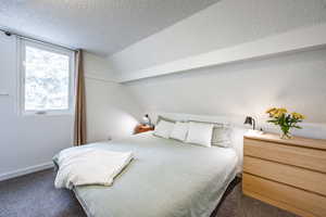 Bedroom featuring a textured ceiling, vaulted ceiling, and dark colored carpet