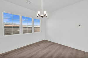 Empty room featuring wood-type flooring and an inviting chandelier