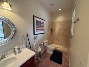 Bathroom featuring toilet, vanity, and tiled shower