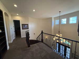 Hallway with dark colored carpet and a notable chandelier