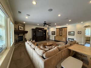 Carpeted living room featuring ceiling fan, a stone fireplace, and crown molding