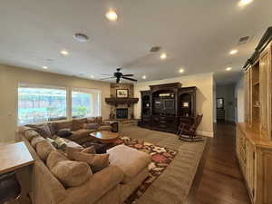 Living room with ceiling fan, a barn door, ornamental molding, a fireplace, and dark hardwood / wood-style flooring