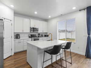 Kitchen with appliances with stainless steel finishes, dark wood-type flooring, sink, a center island with sink, and white cabinetry