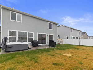 Rear view of property with a yard, a patio, and a hot tub