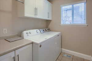 Clothes washing area with cabinets, light tile patterned flooring, and washer and dryer