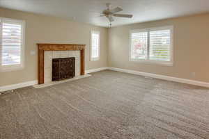 Unfurnished living room with a tile fireplace, light colored carpet, and ceiling fan