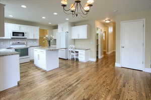 Kitchen with white appliances, hardwood / wood-style flooring, white cabinets, a kitchen island, and hanging light fixtures