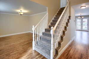 Stairway featuring hardwood / wood-style flooring, crown molding, and a chandelier