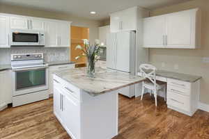 Kitchen with white cabinetry, light hardwood / wood-style floors, and white appliances