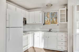 Kitchen with hardwood / wood-style floors, white cabinetry, white appliances, and sink