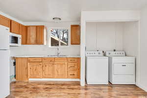 Clothes washing area with independent washer and dryer, sink, and light wood-type flooring