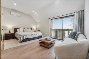 Bedroom with a wall mounted air conditioner, light wood-type flooring, access to outside, and vaulted ceiling