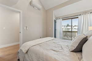 Bedroom with access to exterior, light hardwood / wood-style floors, a wall mounted AC, and lofted ceiling