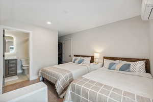 Bedroom with lofted ceiling, ensuite bath, light wood-type flooring, stacked washing maching and dryer, and a wall mounted AC