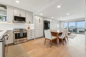 Kitchen with decorative backsplash, white cabinetry, light wood-type flooring, and appliances with stainless steel finishes