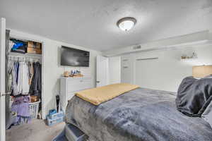 Carpeted bedroom featuring a textured ceiling and a closet