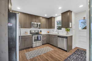 Kitchen with backsplash, sink, light wood-type flooring, and stainless steel appliances