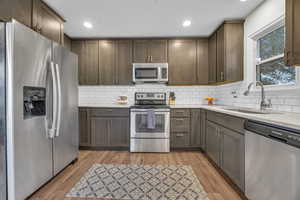 Kitchen featuring tasteful backsplash, sink, light hardwood / wood-style flooring, and appliances with stainless steel finishes