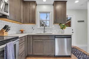 Kitchen featuring sink, light hardwood / wood-style flooring, decorative backsplash, appliances with stainless steel finishes, and light stone counters