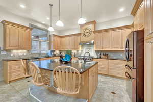 Kitchen with stainless steel appliances, ventilation hood, dark stone counters, decorative light fixtures, and a center island with sink