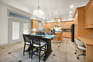 Kitchen with light brown cabinets, pendant lighting, decorative backsplash, black refrigerator, and a center island with sink