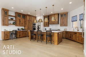 Kitchen featuring light countertops, brown cabinetry, a kitchen island with sink, and pendant lighting