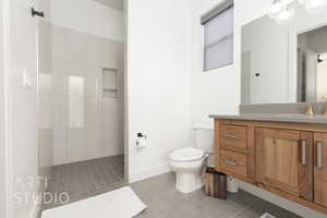 Bathroom with tile patterned flooring, vanity, tiled shower, and toilet