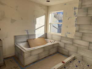 Bathroom featuring a relaxing tiled tub and a textured ceiling